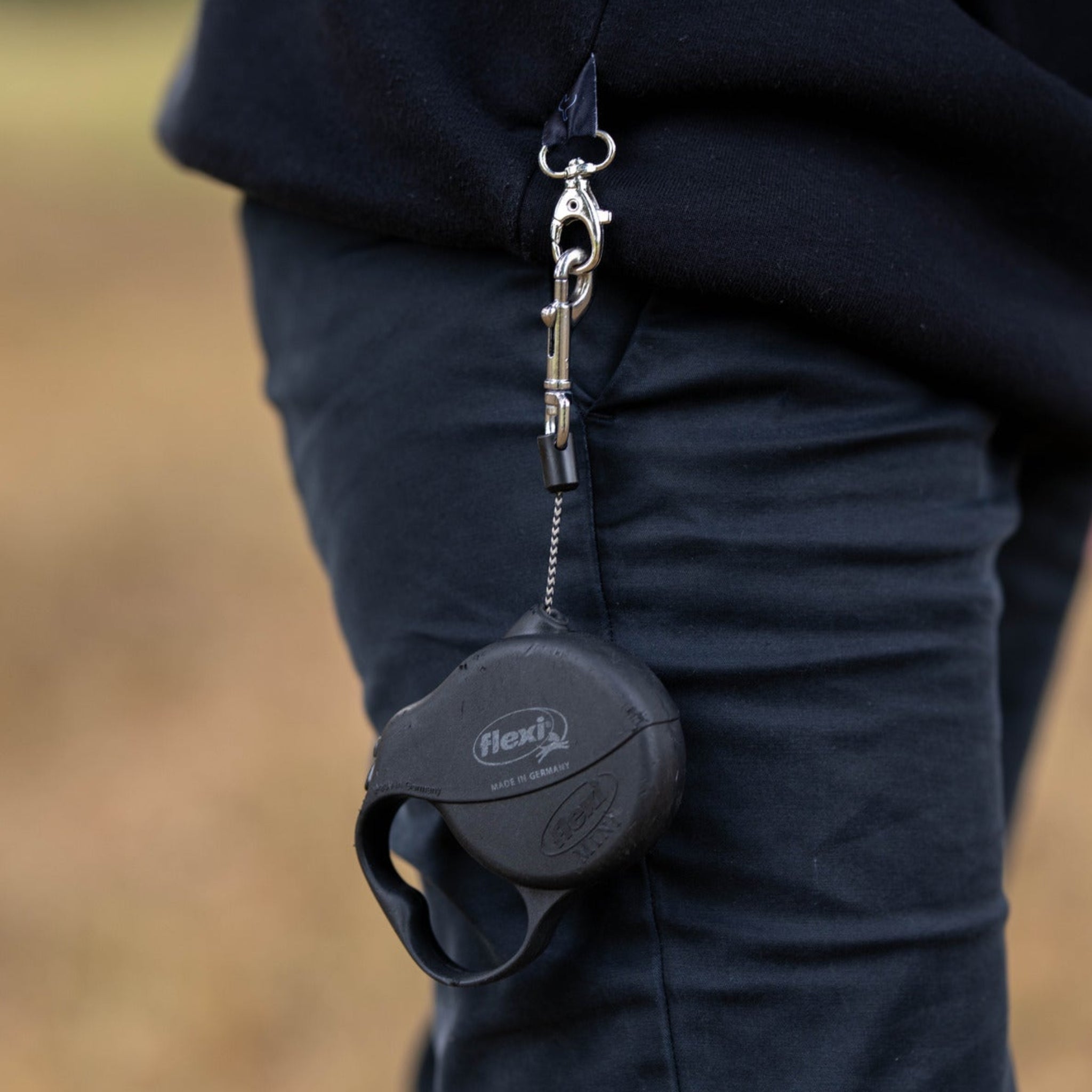 Person wearing a black dog hoodie with a dog lead hanging from the side by the pocket, blurred natural background
