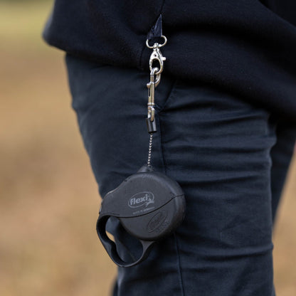Person wearing a black dog hoodie with a dog lead hanging from the side by the pocket, blurred natural background